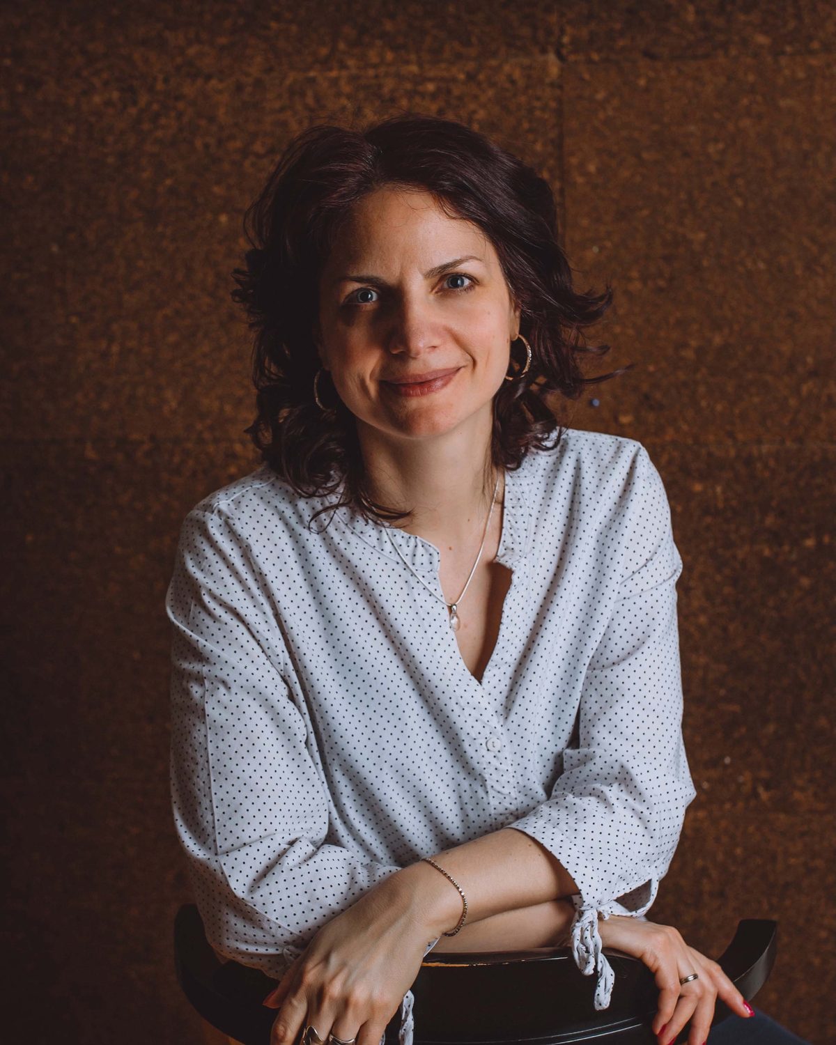 Sanja Rista Popić sedi na stolici i gleda u objektiv, u beloj bluzi sa sitnim tufnama.